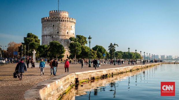 Thessaloniki, Greece - December 24, 2015: People walking on the coast in Thessaloniki next to the white tower which once guarded the eastern end of the city's sea walls