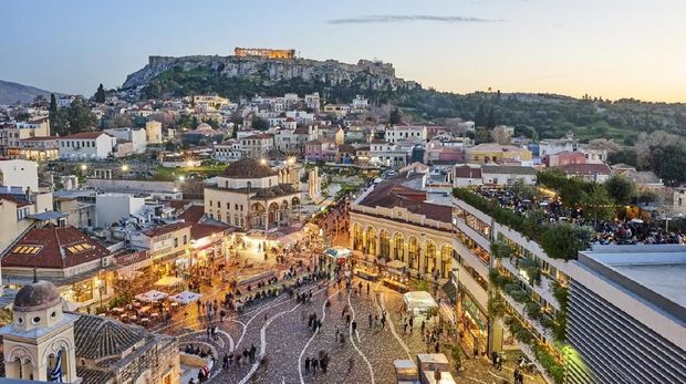 Athens, Greece - February 13, 2016: Aerial view of Athens at sunset with an illuminated Acropolis in the background. In foreground tourists and local people in Monastiraki Square. The clustered homes on the hill is known as Plaka.