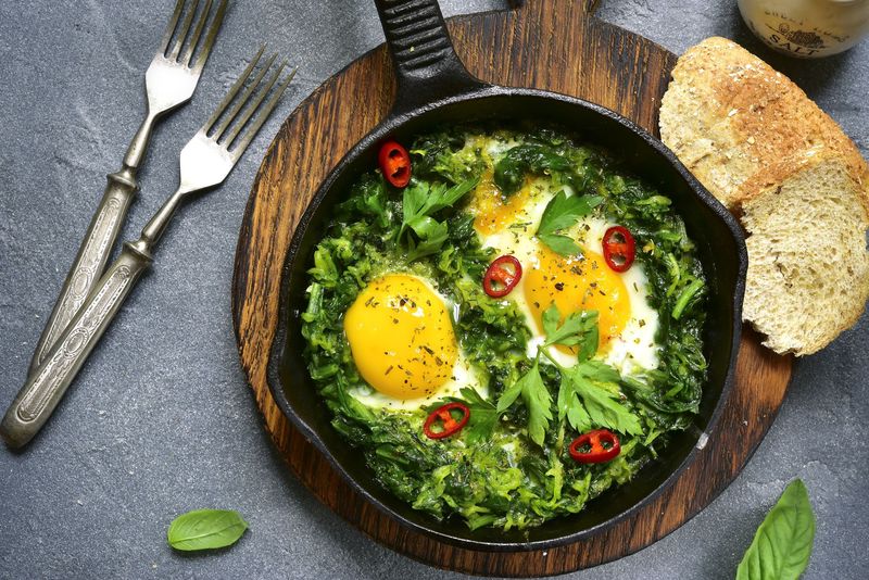 Green shakshuka in a cast iron pan on a grey slate,stone or concrete background.Top view.