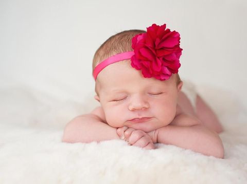 A portrait of a beautiful newborn baby girl wearing a hot pink flower headband. She is sleeping on a cream colored sheepskin rug.
