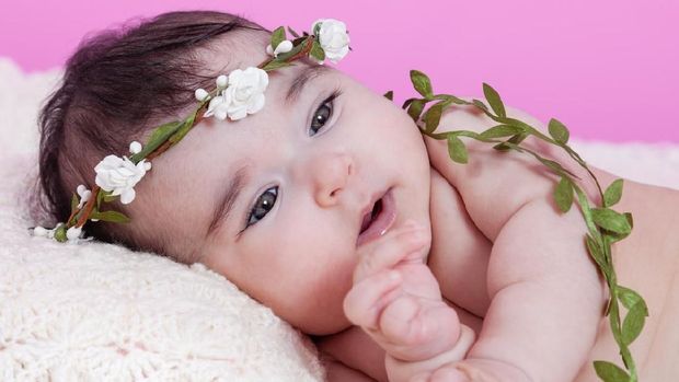 Cute, pretty, happy, chubby and smiling baby girl, laughing with a big smile. Naked or nude with diaper or nappy, wearing a floral wreath headband or headdress. Four months old