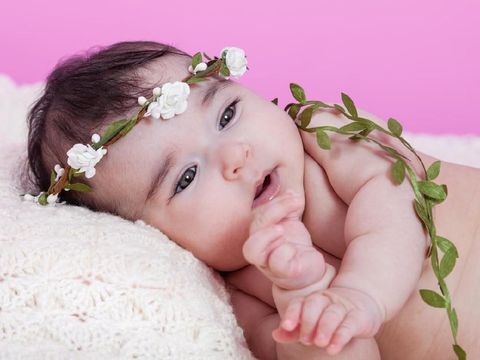 Cute, pretty, happy, chubby and smiling baby girl, laughing with a big smile. Naked or nude with diaper or nappy, wearing a floral wreath headband or headdress. Four months old