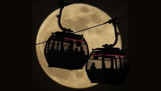 Emirates Air Line cable cars are silhouetted against the backdrop of the 'supermoon' in Greenwich, London, Tuesday, Feb. 19, 2019. Tuesday's full moon, or supermoon, appears brighter and bigger than other full moons because it is close to its perigee, which is the closest point in its orbit to Earth.  (Yui Mok/PA via AP)
