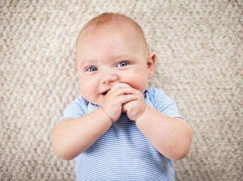 Color image of a baby boy lying on his back on carpet inside a home.