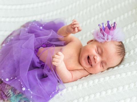 Portrait of newborn baby girl princess with crown sleeping and smiling on soft white blanket.