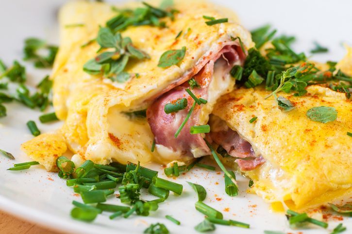 A photo of an omelette with cherry tomatoes, parsley. and grated cheese, shot from above on a rustic wooden texture with a place for text