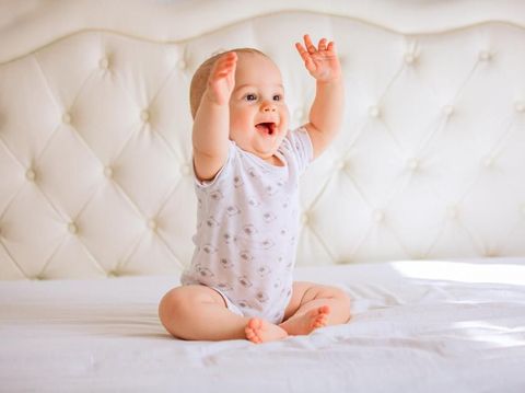 Cute baby boy in white sunny bedroom.