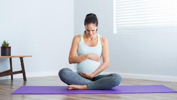 Pregnancy yoga meditation. Full length healthy 8 months pregnant calm Asian woman meditating or doing yoga exercise at home. Relaxation yoga sitting side stretch positions.