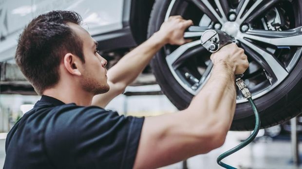 Handsome mechanic in uniform is working in auto service. Car repair and maintenance. Twisting/untwisting bolts on wheel.