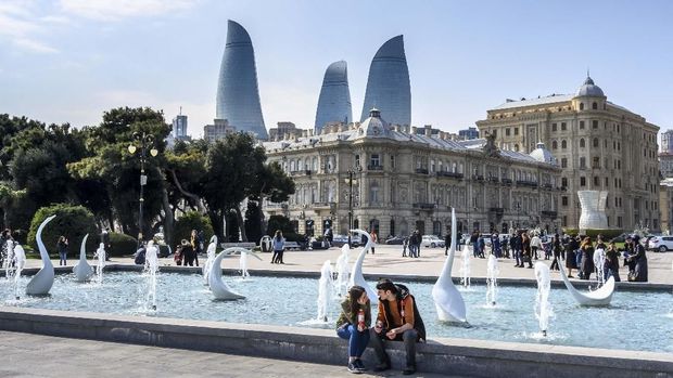 A couple sits on a fountain in the center of Baku, with the Flame Tower seen in the background, on March 22, 2019. (Photo by Mladen ANTONOV / AFP)