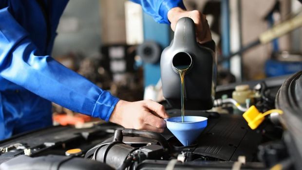 Male mechanic refilling car oil in service center