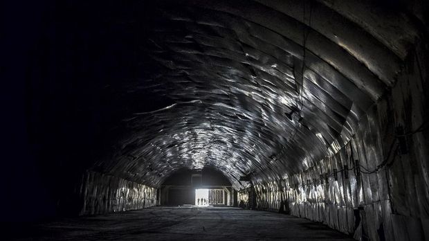 Albanian military personnel walks out of the main tunnel of the Gjader Air Base built near the city of Lezhe, on February 5, 2019. - On a barren hillside in northern Albania lies a portal to the country's communist past: a massive steel door creaks open to reveal a hidden former air base burrowed into the heart of the mountain. Made up of 600 metres (1,980 feet) of tunnels that once teemed with military life, the secret Gjader air base is now a depot for dozens of hulking communist-era MiG jets collecting dust in the darkness. Three decades after shedding communism, Albanian authorities are still trying to sell off the Soviet and Chinese-made aircraft, of which there are dozens more in another nearby air base. (Photo by Gent SHKULLAKU / AFP)