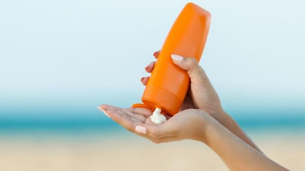 Woman hand apply sunscreen on the beach