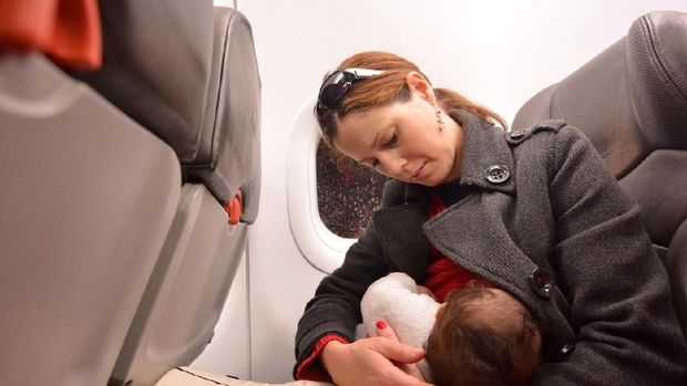 Mother breastfeeding her newborn baby during flight. Concept photo of air travel with baby.