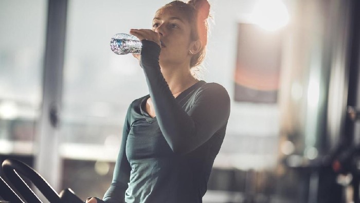 Tired female athlete drinking fresh water while resting from exercising class in a health club.