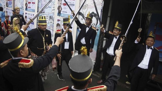 Petugas Kelompok Penyelenggara Pemungutan Suara (KPPS) menyambut warga yang akan menggunakan hak pilihnya dengan prosesi pedang pora di TPS 27 Kampung Happy, Manahan, Solo, Jawa Tengah,