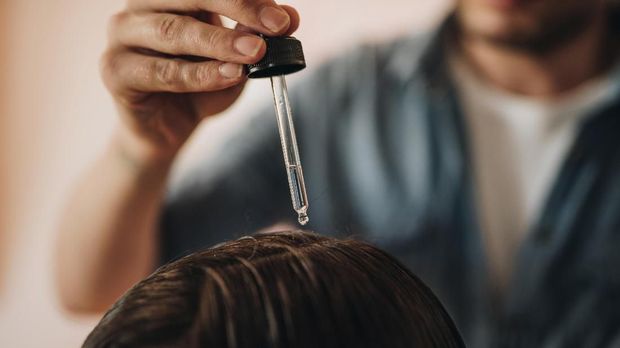 Close up of a hairdresser applying hair oil on customer's hair at the salon.