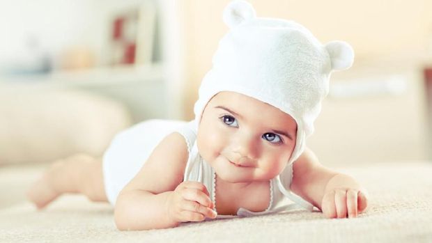 Little baby girl lying on bed,smiling and looking at camera.She got teddy bear hat on head.