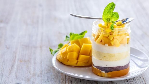 Sweet homemade Mango dessert, cheesecake, trifle, mouse in a glass jar on a light wooden background