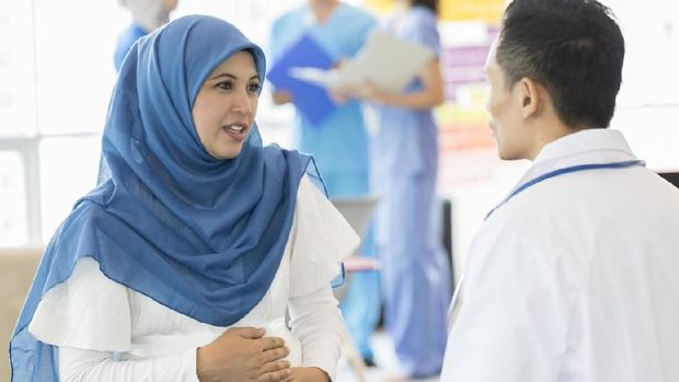 Maternity patient talks with ob/gyn holds her abdomen while discussing something with doctor during prenatal appointment.