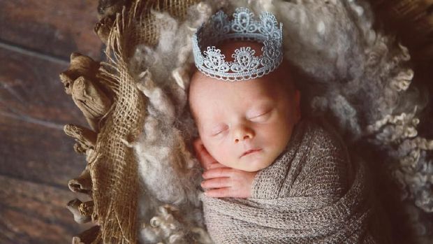 A newborn baby boy smiles as he wears a silver crown. A prince is born!