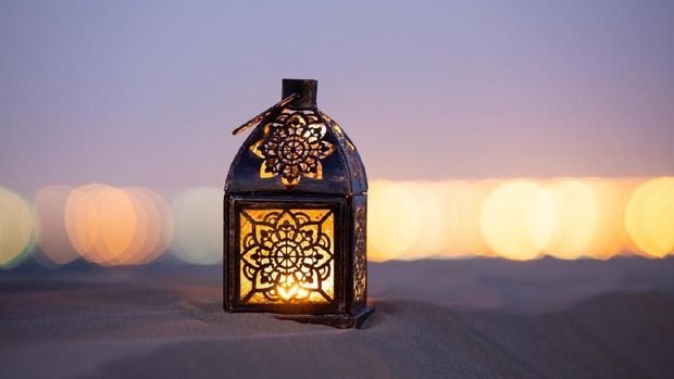 Traditional ornamental arabic lantern with a burning candle in desert after sunset during blue hour. Festivel greeting card for Ramadan Kareem and Ramadan Mubarak. Dubai, UAE.