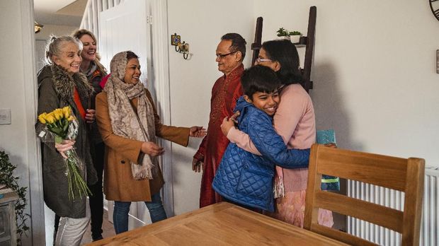 A family greet one another with gifts. The senior man is wearing a kurta/salwar kameez. The senior woman is also wearing a duppatta.