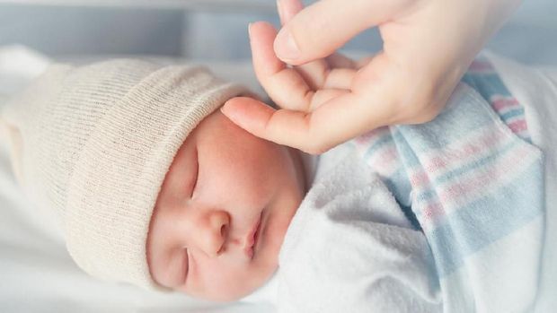 Mothers hand comforting new born baby boy sleeping.