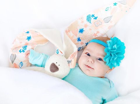 Close-up of adorable cute newborn baby girl of two months on white background. Lovely child playing with plush rabbit toy wigh bit long ears. Holiday, Easter, childhood concept.