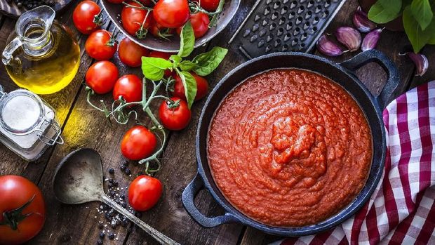 Preparing tomato sauce at home. Top view of a rustic wooden table filled with fresh ingredients for preparing tomato sauce at home. Ingredients for preparing tomato sauce are fresh ripe tomatoes, basil, olive oil, garlic, salt and pepper. The ingredients are scattered on the table all around a cast iron pan filled with prepared tomato sauce. Predominant color is red. DSRL studio photo taken with Canon EOS 5D Mk II and Canon EF 100mm f/2.8L Macro IS USM