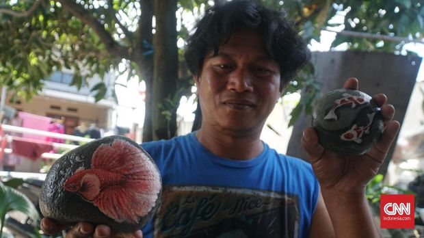 Mang Obe memamerkan lukisan di atas batu.