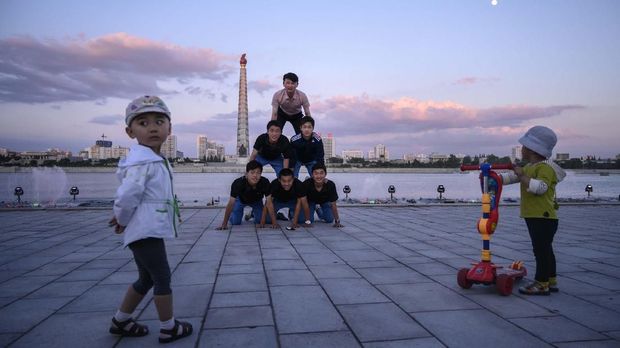 In a photo taken on June 15, 2019 children watch as a group of Korean visitors from Japan perform a gymnastic routine on banks of the Taedong river before the landmark Juche tower in Pyongyang. (Photo by Ed JONES / AFP)