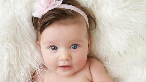 Newborn baby girl posed in a bowl on her back, on blanket of fur, smiling looking at camera