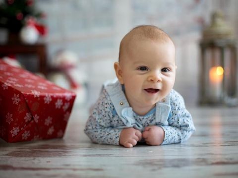 Cute christmas portrait of little baby boy, lying on his belly on the floor, smiling happily, christmas decoration and presents around him