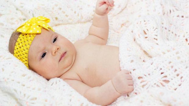 Two month infant girl is lying on knitted blanket with ribbon on head