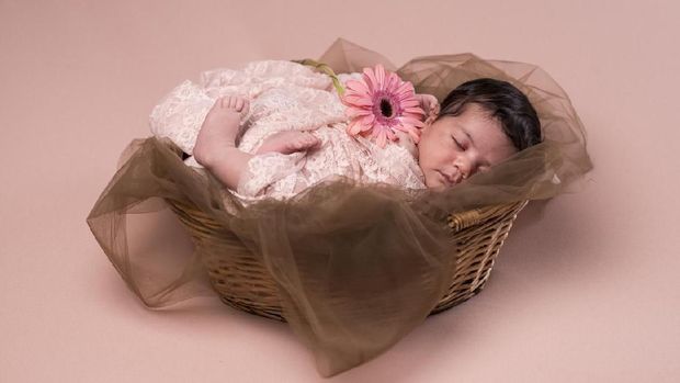 Portrait of a sleeping, 2 week old newborn baby girl wearing frilly, lavender purple bloomers and a pearl headban. Shot in the studio on a white blanket.