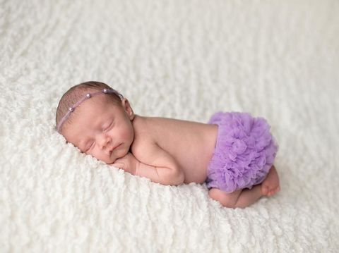 Portrait of a sleeping, 2 week old newborn baby girl wearing frilly, lavender purple bloomers and a pearl headban. Shot in the studio on a white blanket.