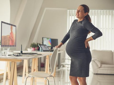 Pregnant mid adult woman standing by the desk in the office, having back pain at the end of pregnancy.