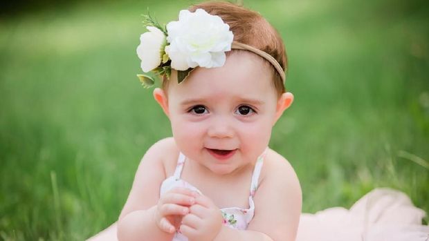 Cute one year old caucasian girl outside in grass wearing a pink summer dress and floral headband