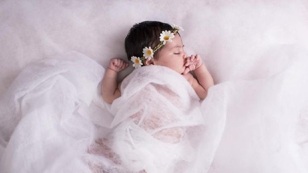 2 weeks newborn baby girl sleeping on a wool fabric, wearing chamomile flower headband.