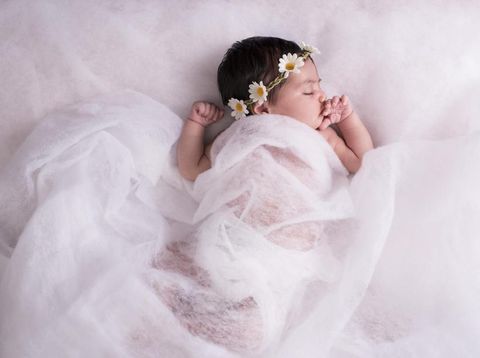 2 weeks newborn baby girl sleeping on a wool fabric, wearing chamomile flower headband.