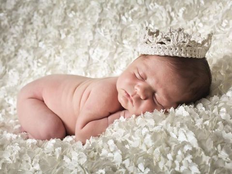 Newborn baby boy sleeping sleeping in a comfortable blanket wearing a white crown