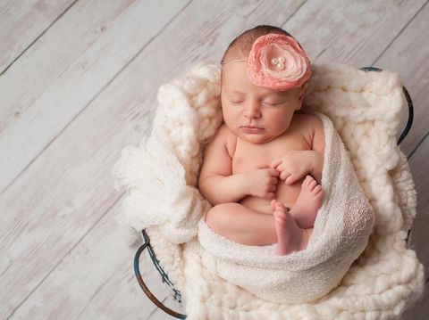 A portrait of a beautiful, two week old, newborn baby girl wearing a crocheted bonnet. She is smiling and sleeping on yellow colored fabric.