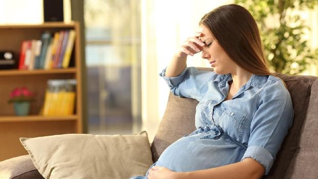 Worried pregnant woman sitting on a couch in the living room at home