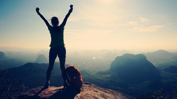 silhouette of cheering woman hiker open arms at mountain peak