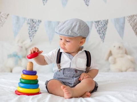 Cute toddler child, baby boy, playing with colorful toy in sunny bedroom, flag banner decoration behind him