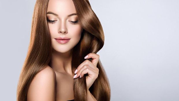 Young, brown haired woman  with voluminous hair.Beautiful model with long, dense, straight hairstyle and vivid makeup, is touching own hair with tenderness. Symbol of attentiveness to hair and good care of it. Incredibly dense, wavy,and shiny hair.