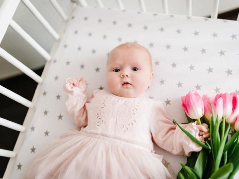 Close-up of newborn baby girl hand holding a bouquet of flowers pink tulips. New life, love and holiday concept. Women's Day. Mother's Day. flat lay. top view.