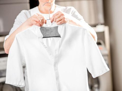 Senior washwoman hanging a shirt on the hanger standing in the professional laundry