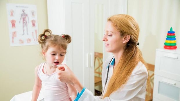 Pediatrician woman giving medicament to little girl with a spoon. Kid is opening mouth. Hospital room on the background.